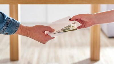 dłonie kobiety i mężczyzny koperta z banknotami pod stołem przekazywana