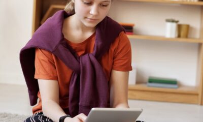 photo of girl using tablet while sitting on carpet