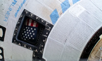 The American flag pictured inside the window of Boeing’s Starliner spacecraft at the International Space Station. Credit: NASA