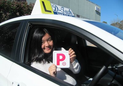 Student smiling behind the wheel inside a D-Tech Driver Training car holding her red P-plate after passing her test in Blacktown.