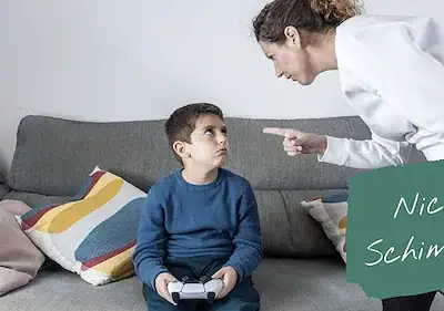 Mutter zeigt mit dem Finger auf Kind mit Gaming-Controller auf Sofa, grüne Tafel mit Text "Nicht schimpfen"