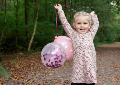 Blij meisje in het bos bij Ockenburgh speelt met roze ballonnen tijdens een gezinsshoot