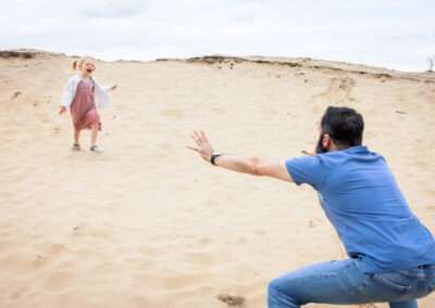 Papa staat klaar om zijn blonde dochtertje te vangen die van een duin afrent
