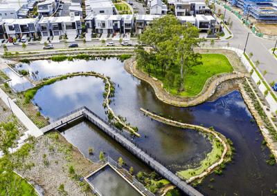 Aerial view of a modern suburban development with white townhouses along a curved waterway and a green park area nearby.