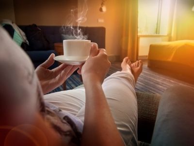 Eine Frau sitzt gemütlich auf dem Sofa und hält eine Tasse dampfenden Kaffee