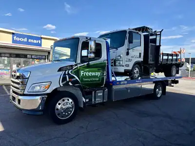 Freeway Towing & Storage flatbed truck hauling an Isuzu NPR commercial work truck in Phoenix, AZ