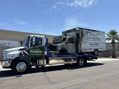 Freeway Towing & Storage flatbed truck hauling a fire-damaged box truck in Phoenix, AZ