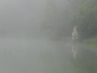 Dunst über einem See, am anderen Ufer eine Statue.