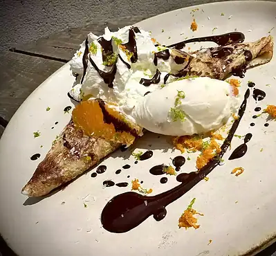 Crêpe dorée et croustillante servie dans une assiette rustique, garnie de fruits frais, d’un filet de chocolat fondant et d’une boule de glace vanille. Une spécialité gourmande de la crêperie Léon et Suzette à Moncoutant-sur-Sèvre, à seulement 15 minutes de Bressuire.
