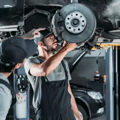 Mechanic inspects exposed brake rotor under lifted vehicle while mercedes auto repair diagnosis continues