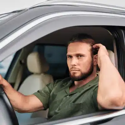 Concerned driver sits in car, scratching head at Mercedes-Benz service center, awaiting diagnostics and advice