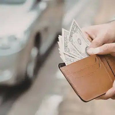 Person holds wallet with cash near car, budgeting after Land Rover service appointment repair estimate