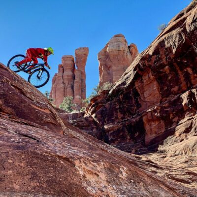 1 Tracy cathedral background (1) Mountain biker riding red rock trails in Sedona, Arizona with Cathedral Rock spires in the background under a clear blue sky.