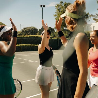 Group of women celebrating on tennis court, waving and high-fiving after a successful team match Group of women celebrating on a tennis court, waving and high-fiving each other after a successful team match. Happy and supportive sports environment.