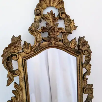 Miroir ancien vertical avec cadre en bois et stuc doré richement sculpté de motifs rocaille, volutes et fronton