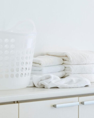Stack of clean bath towels on a white dresser with a bottle of natural laundry detergent