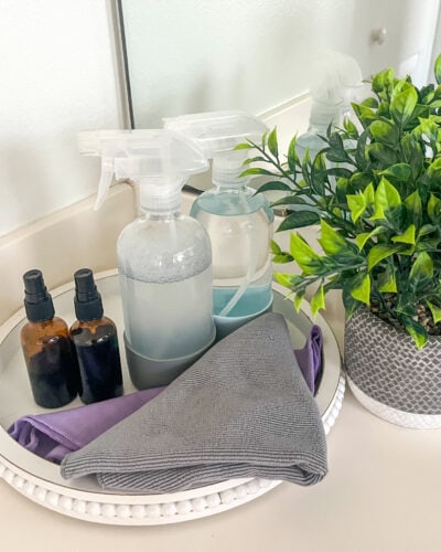 picture of natural cleaners in glass bottles on top of a bathroom counter with a fake plant in the background