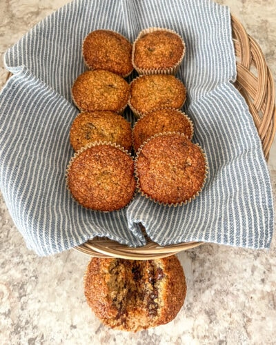 Fresh milled flour banana bread muffins nestled in a basket lined with a soft blue kitchen towel, golden brown with domed tops and a tender crumb, made with ripe bananas for a wholesome, homemade feel.