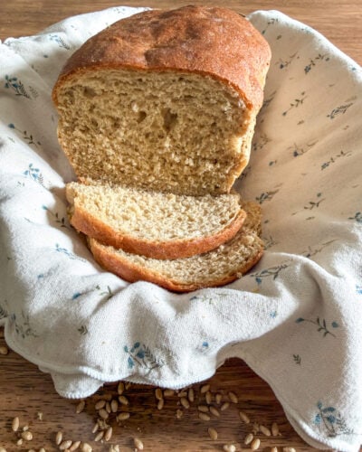 Fresh milled bread with Khorasan and hard white wheat in a basket with a neutral colored kitchen towel on top of a wooden table with wheat berries scattered around.