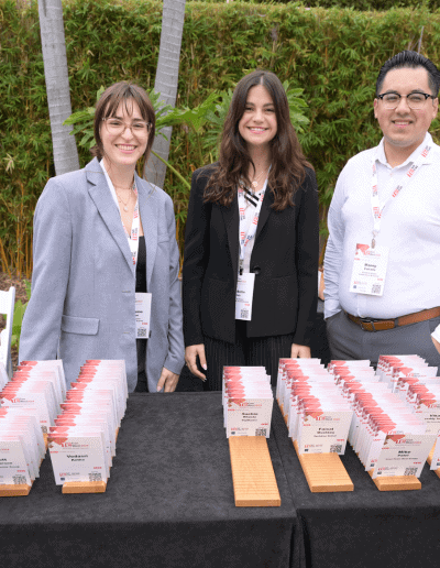 hree CTC team members standing behind the registration check-in desk at the TiE SoCal 2024 event, smiling and ready to assist attendees