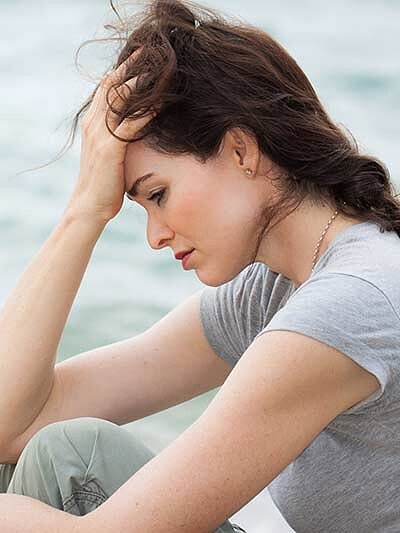 A woman sitting on the beach, looking distressed as she rests her head in her hands, seeking solace and contemplation.