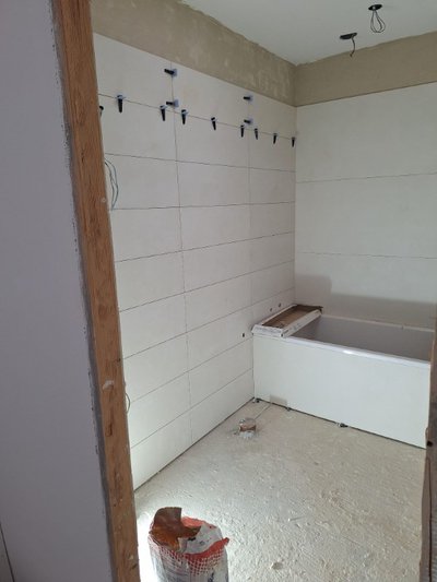 Interior de baño en reforma en Menorca, paredes con azulejos blancos, bañera empotrada y zona de instalación de grifería en progreso, mostrando materiales expuestos y preparación de revestimientos