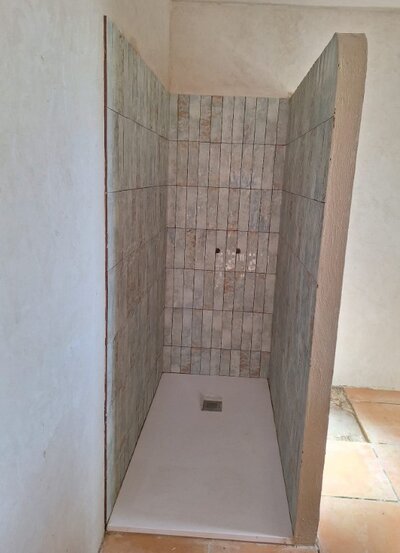 Alicatado y revestimiento cerámico gris de formato rectangular en tono suave, instalado en una ducha o cabina con paneles laterales, ubicado en Menorca