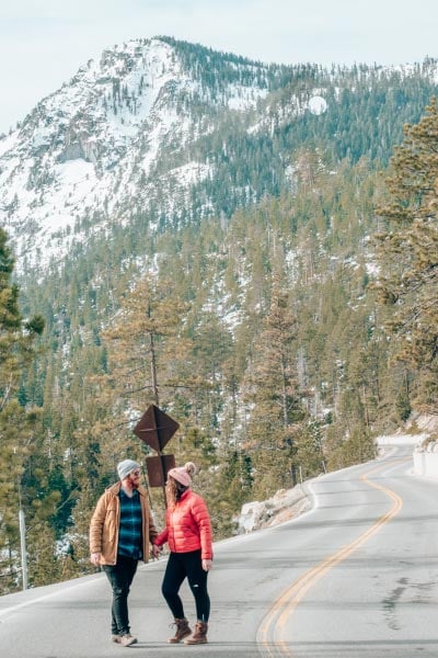 Couple on a road in front of snowy mountains covered with pine trees in Lake Tahoe, California.