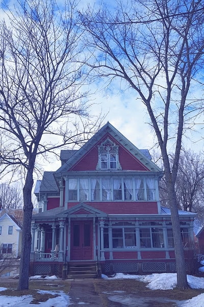 Two tall, leafless trees frame a large red house. The atmosphere is foreboding. 