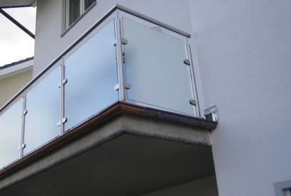 Modernes Balkongeländer von Stahl- und Metallbau Drost aus Edelstahl mit mattierten Glasfüllungen, montiert an einem Gebäude mit weißer Fassade.