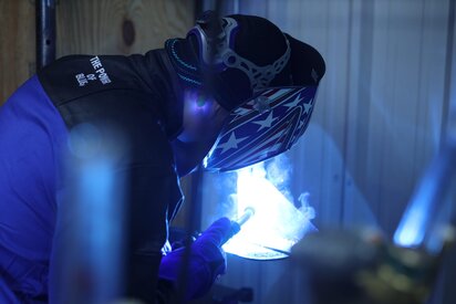 Welder welding with a stars and stripes helmet, Miller welding jacket