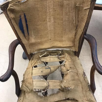 Old armchair with torn fabric and exposed wiring, vintage furniture repair needed.