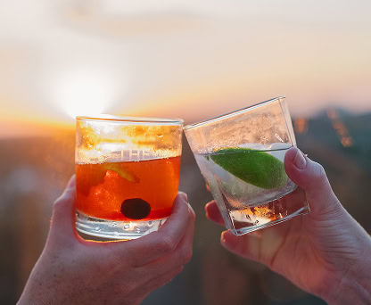 Two hands clink cocktail glasses, celebrating a sunset happy hour on the patio of a luxury Raleigh condo