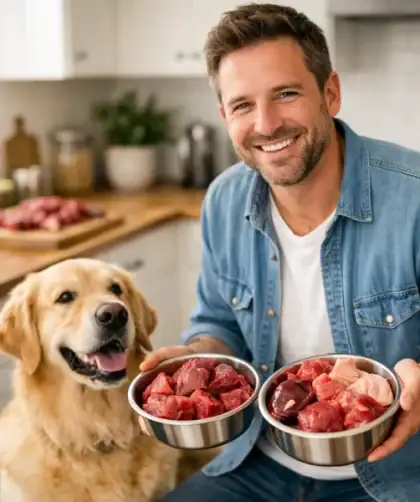 Propriétaire souriant tenant des portions de viande crue fraîche pour son chien Golden Retriever en bonne santé dans une cuisine moderne.