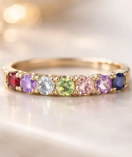 Gros plan sur une bague en or ornée de plusieurs pierres de naissance colorées disposées harmonieusement, lumière douce mettant en valeur les couleurs des gemmes.