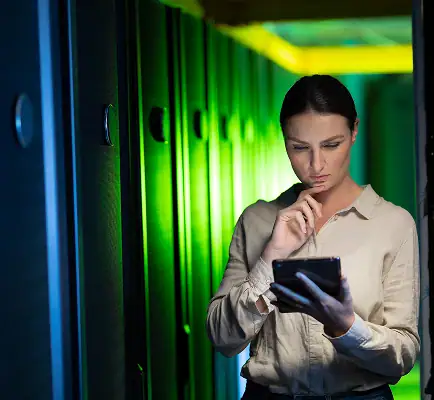 Cybersecurity professional reviewing data on a tablet in a server room with green-lit server racks