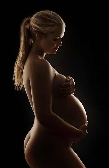Elegant gravidfotografi av en gravid kvinne med spotlight-belysning, som fremhever den naturlige skjønnheten og formen. Perfekt for gravide fotosessions og minneverdige øyeblikk under svangerskapet.