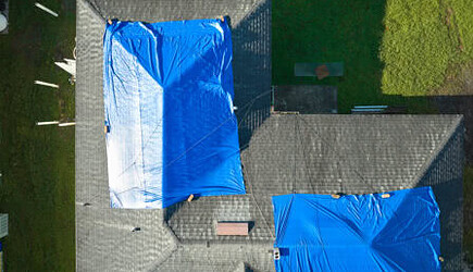 Top view of leaking house roof covered with protected roof tarp sheets against rain water leaks until replacement of asphalt shingles. Damage of building rooftop as aftermath of hurricane Ian in Florida
