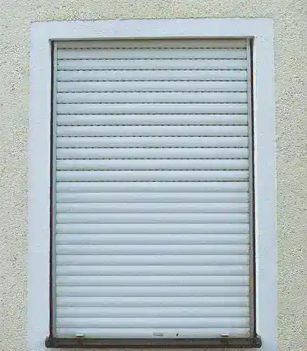 Vista frontale di una tapparella avvolgibile chiusa installata su una finestra esterna con muro intonacato chiaro.
