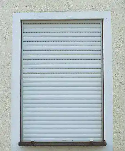 Vista frontale di una tapparella avvolgibile chiusa installata su una finestra esterna con muro intonacato chiaro.