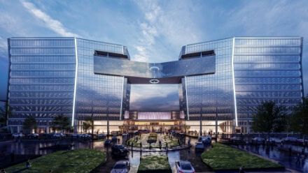 An exterior view of two modern office towers with mirrored exteriors, joined by an oculus bridge that overlooks a Raleigh park in Midtown