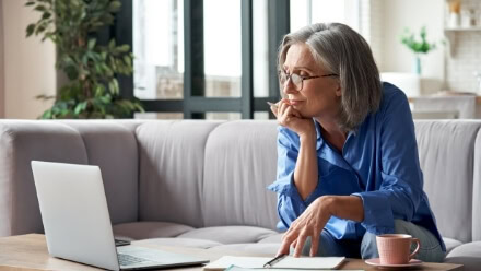 A well-dressed professional woman browses on her laptop in the living room of her luxury Raleigh apartment