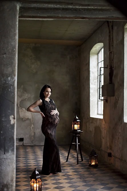 Mamma med gravid mage i en rustikk innendørs setting, fotografert i en kunstnerisk gravidfotografering for spesielle minner.