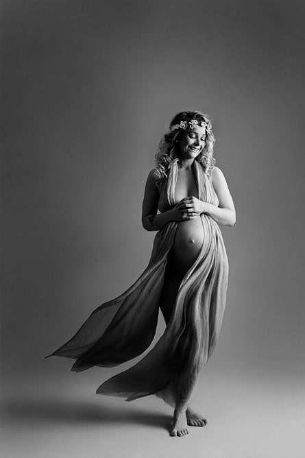 Elegant gravidfotografering av gravid kvinne med flytende stoff og blomsterkrans, portrett i svart-hvitt for å fremheve skjønnheten ved svangerskapet.