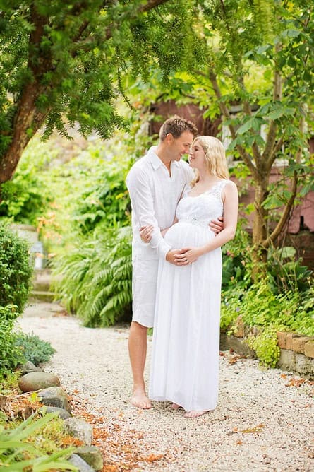 Nydelig gravidfoto av et par i en grønn hage, fotografert i naturlig lys. Perfekt for gravidyoga eller familiefotografering, viser kjærlighet og forventning i vakre omgivelser.