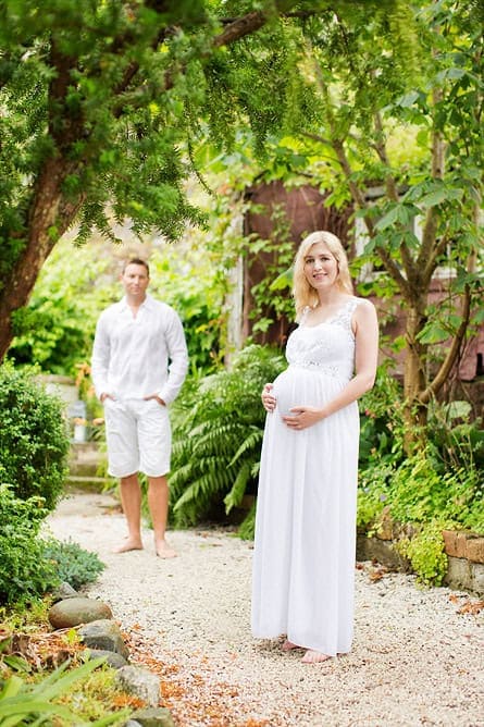 Nydelig gravidfotoseksjon i en grønn hage med glade foreldre.