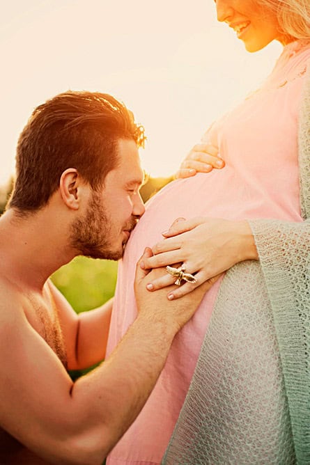 Kjærlig gravidfotografi av par som nyter øyeblikket foran en solnedgang, vekt på kjærlighet og forventning til babyen. Perfekt for gravidfoto og familiebilder i graviditetshistorier.