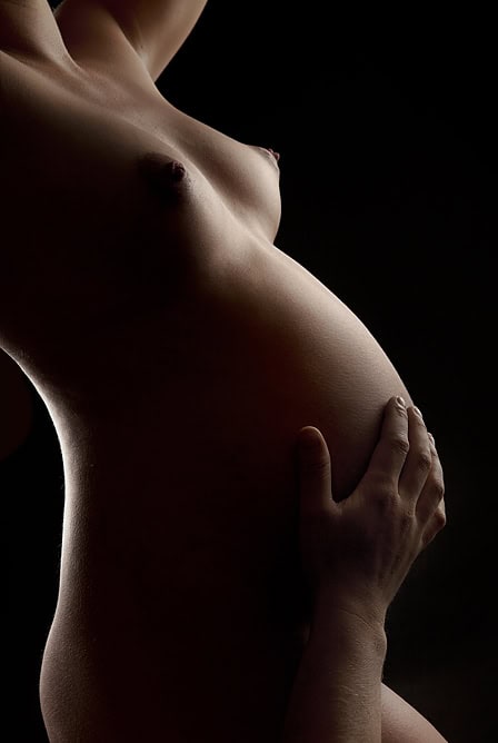 Elegant gravidfoto av en gravid kvinne med myk belysning for en intim og kunstnerisk følelse, perfekt for gravidfotografering og minner om svangerskapet.