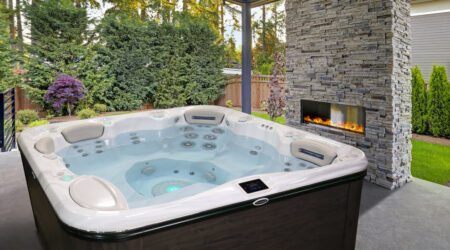 Un spa est installé sur une terrasse, dans un jardin, près d'un poêle extérieur.