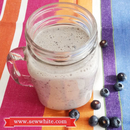 Honey and banana milkshake in a glass with blueberries around it